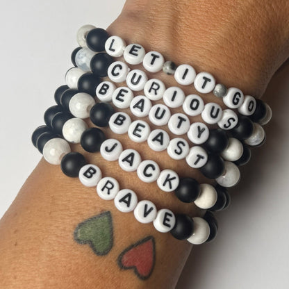 Stack of bracelets with lettered beads on a wrist against a white background